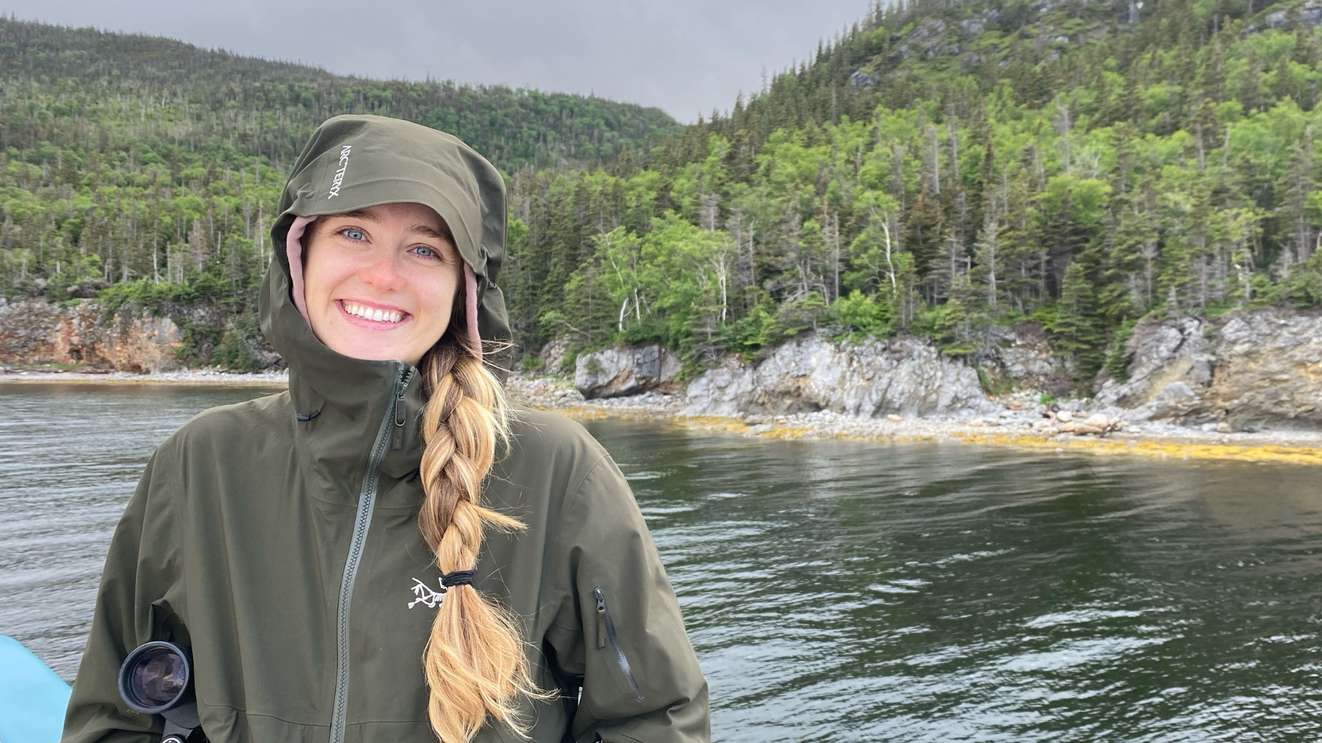 Siobhan Finan wears a black rain jacket on a boat with water and trees in the background.
