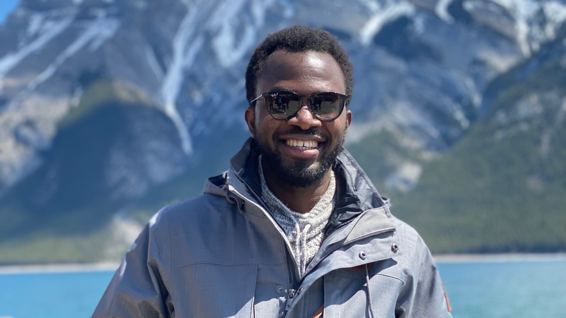 Yemi stands in front of blue lake and mountains