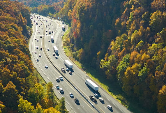 Cars driving along highway located between thick forests