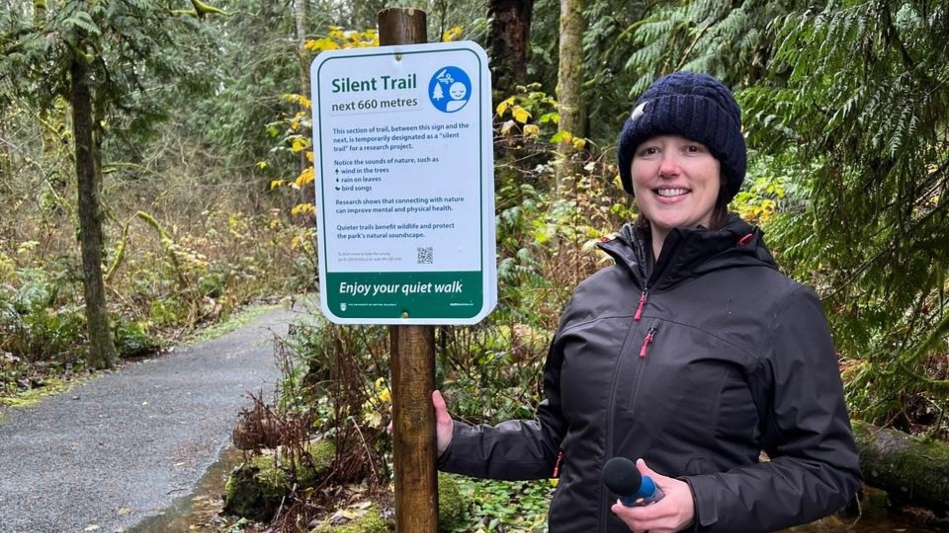 Tara Brown stands next to a sign in the forest indicating a new silent trail.